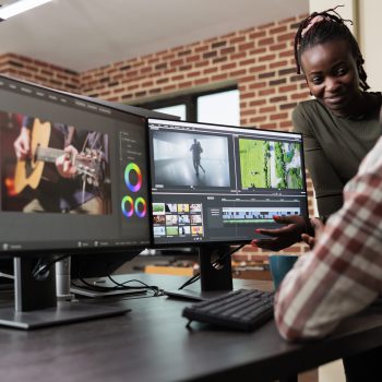 Post production department leader advising colleague to improve colors and frames quality of footage. Creative professional video editors collaborating in order to finish film project upon deadline.
